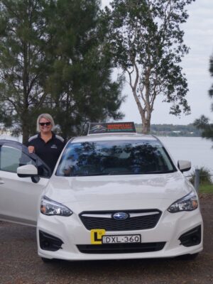 A woman sitting in front of a white car.